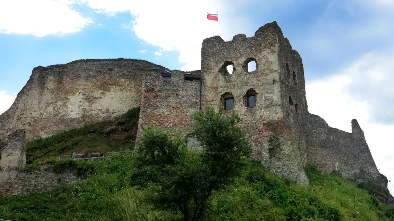 Ruiny zamku Czorsztyn na wzgórzu, z polską flagą powiewającą na wieży.