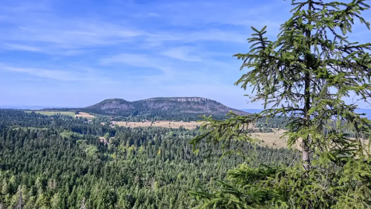 Widok na górzysty krajobraz z lasami i polami, w oddali widać płaskie wzgórze przypominające fort Karola.