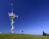 Wieża widokowa z krzyżem na górze Grzywackiej, z krętymi schodami i antenami, na tle błękitnego nieba.