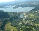 Widok z lotu ptaka na zapora wodna w Myczkowcach, otoczona zielonymi wzgórzami i rozległym jeziorem.