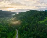 Mglista dolina w Bieszczadach, gdzie kręta droga wije się wśród gęstych lasów. Słońce przebija się przez chmury, tworząc magiczną atmosferę.