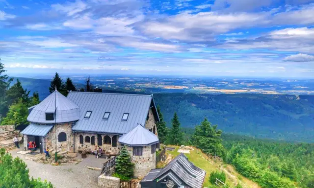 Kamienny budynek na szczycie góry, z którego roztacza się widok na rozległą dolinę. Wysoki kamień stanowi część architektury.