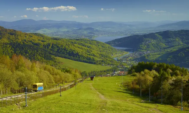Widok na zielone beskid mały szczyty, jezioro i miasteczko. Kolejka krzesełkowa wjeżdża na górę.