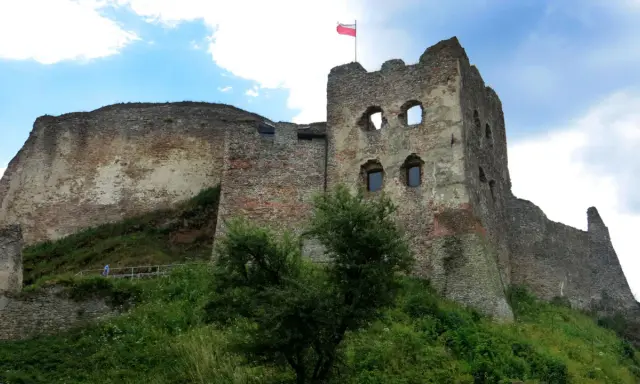 Ruiny zamku Czorsztyn na wzgórzu, z polską flagą powiewającą na wieży.