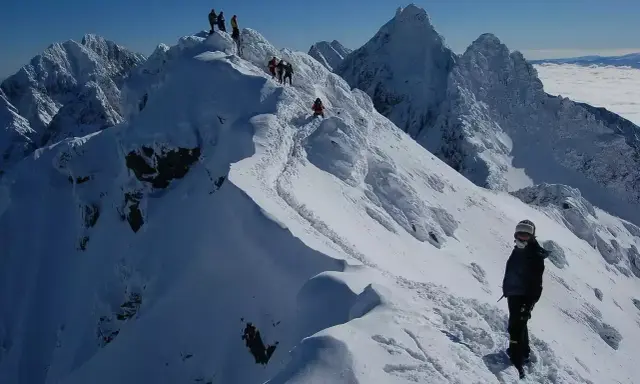 Zimowy trekking po graniach Tatr, gdzie śnieg tworzy prawdziwą koronę gór polskich. W oddali widać morze chmur.