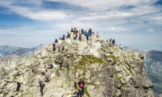 Tłum turystów na skalistym szczycie Rysów, podziwiający panoramę Tatr.
