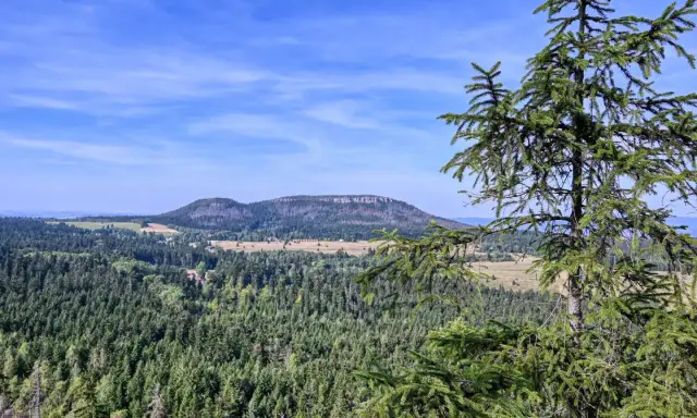 Widok na górzysty krajobraz z lasami i polami, w oddali widać płaskie wzgórze przypominające fort Karola.