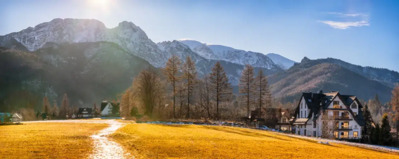 Złota polana prowadzi do górskiej miejscowości u stóp ośnieżonych szczytów. Widok na Giewont i trasę turystyczną.