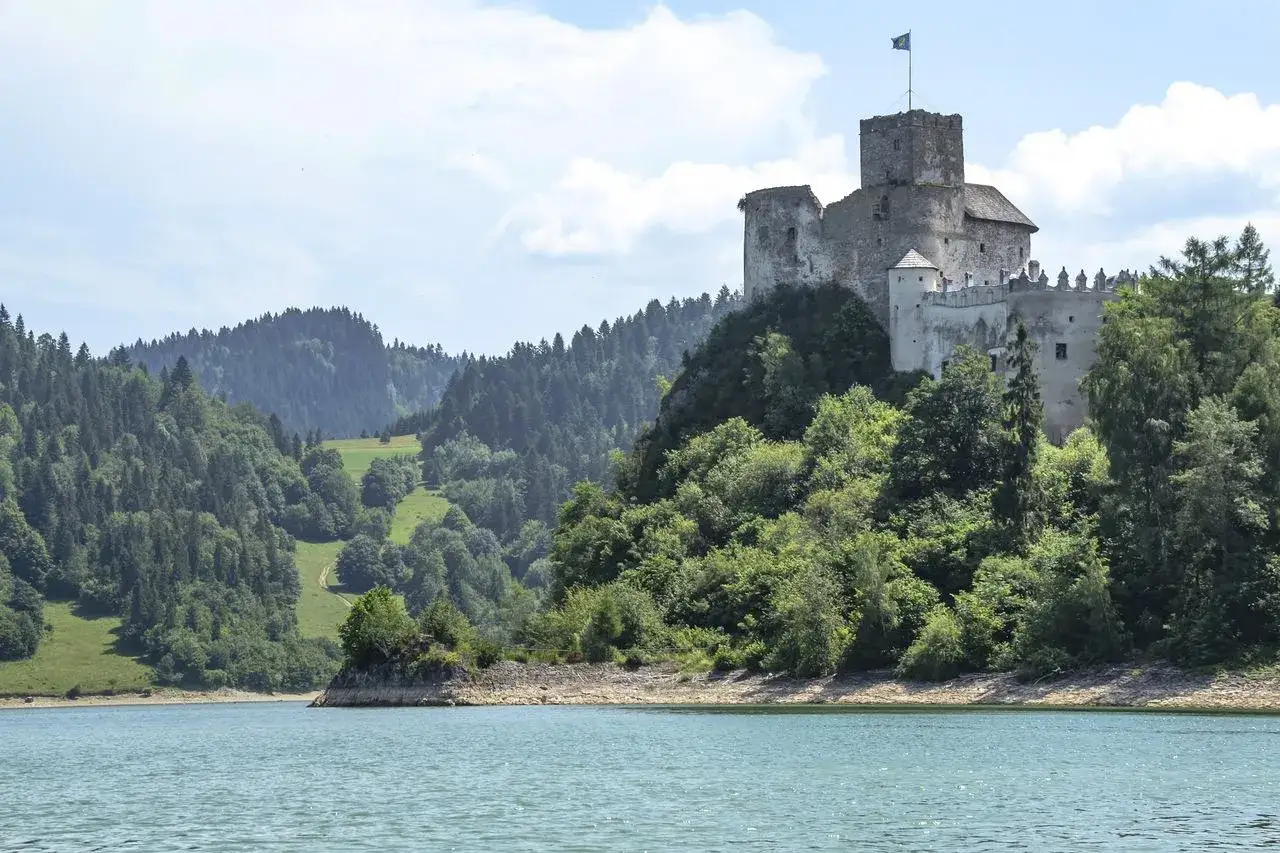 Zamek Czorsztyn góruje nad jeziorem, otoczony zielonymi wzgórzami i lasami.