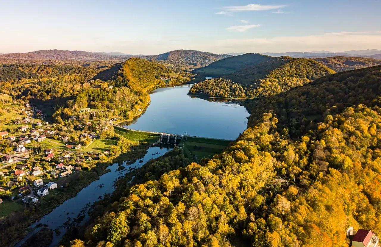 Jesienna panorama z lotu ptaka na zapora wodna w Myczkowcach, otoczona złotymi lasami i malowniczą wsią.