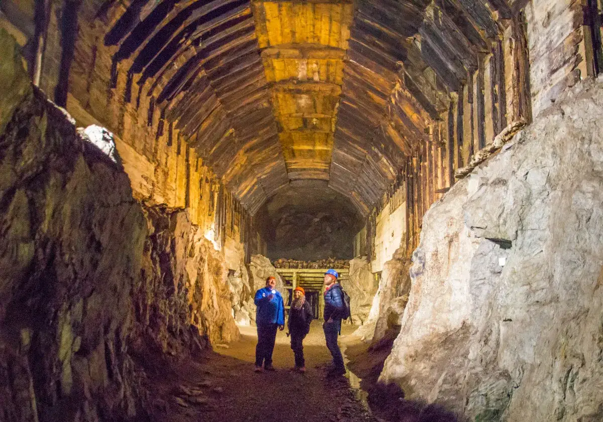 Trzech turystów w kaskach eksploruje mroczny tunel. To fascynujące riese zwiedzanie, gdzie drewniane wsporniki tworzą sklepienie.